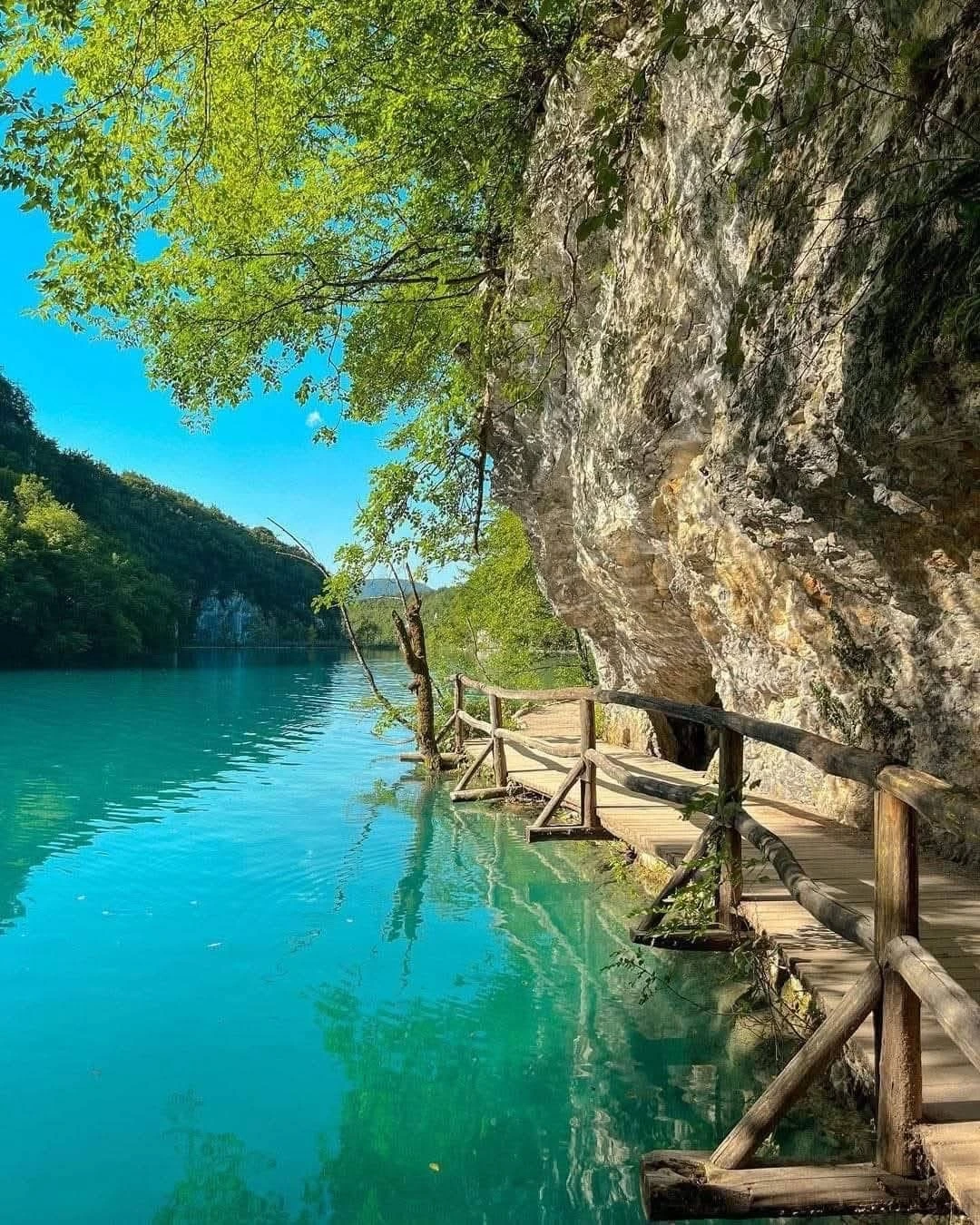 A wooden cliffside boardwalk hugging the travertine wall above an emerald lake at Plitvice Lakes National Park, Croatia